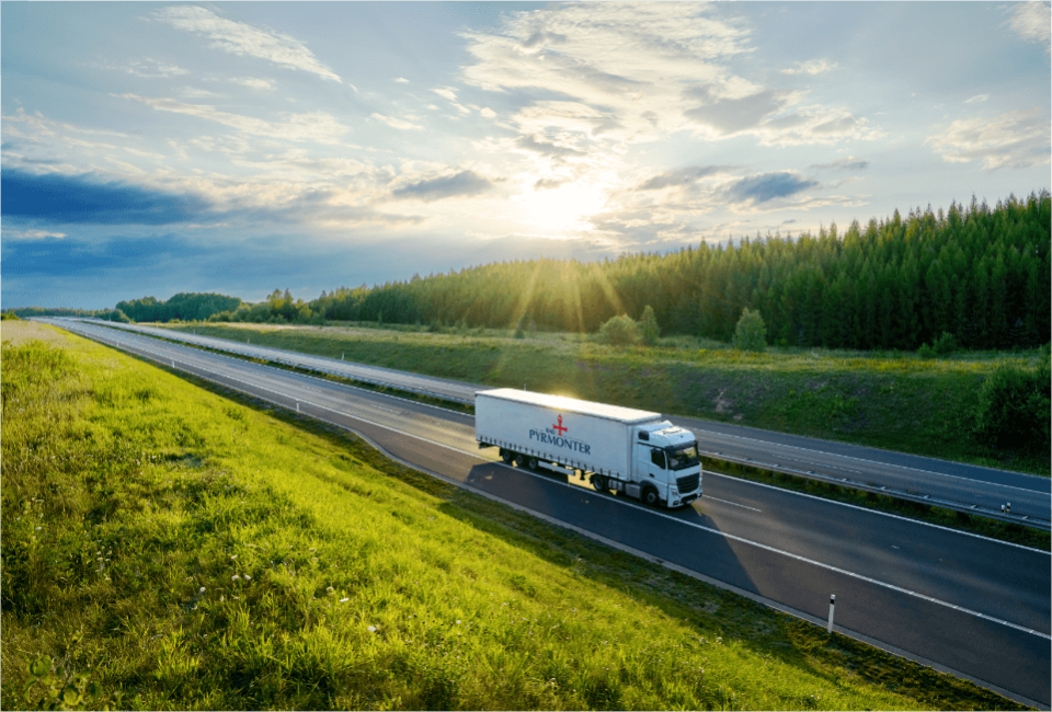 Ein Bad Pyrmonter LKW fährt auf einer Autobahn durch grüne Landschaft bei Sonnenuntergang.