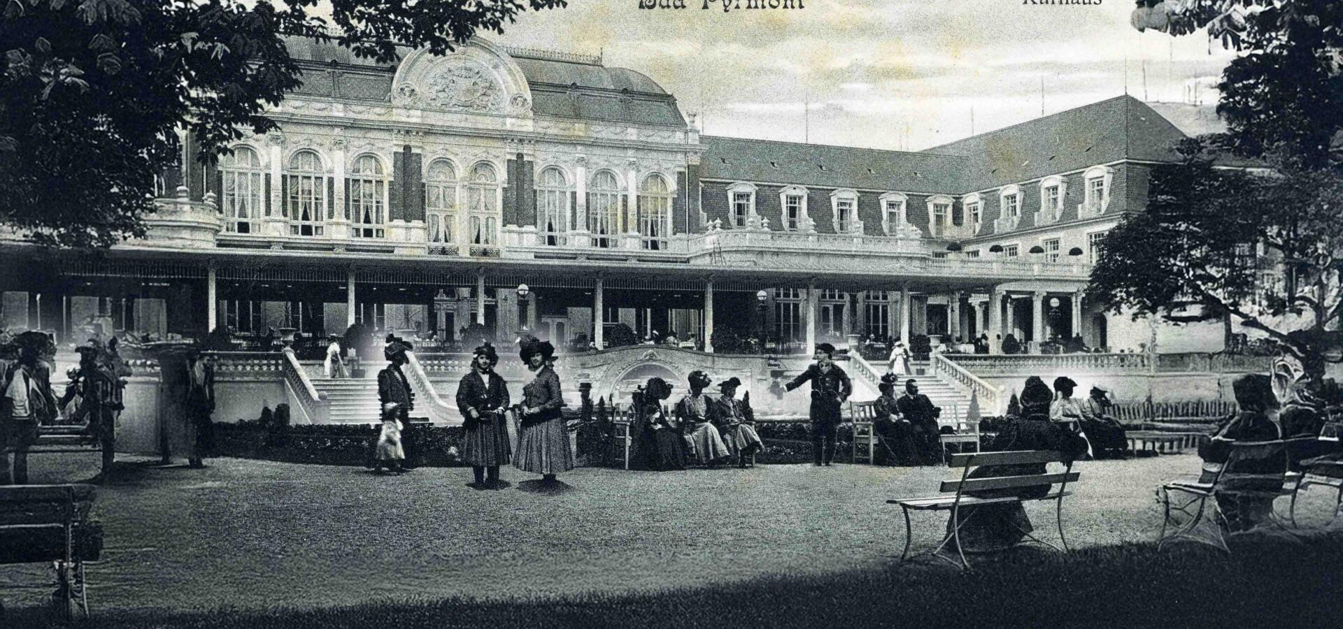 Alte Schwarz-Weiß-Aufnahme des Kurhauses in Bad Pyrmont mit Besuchern im Park.