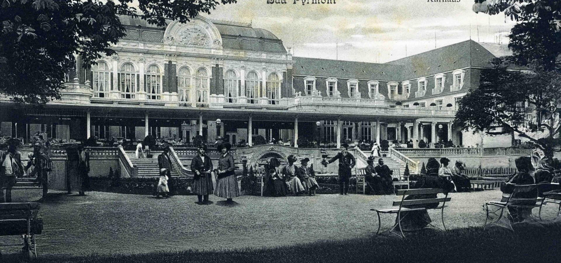 Alte Schwarz-Weiß-Aufnahme des Kurhauses in Bad Pyrmont mit Besuchern im Park.