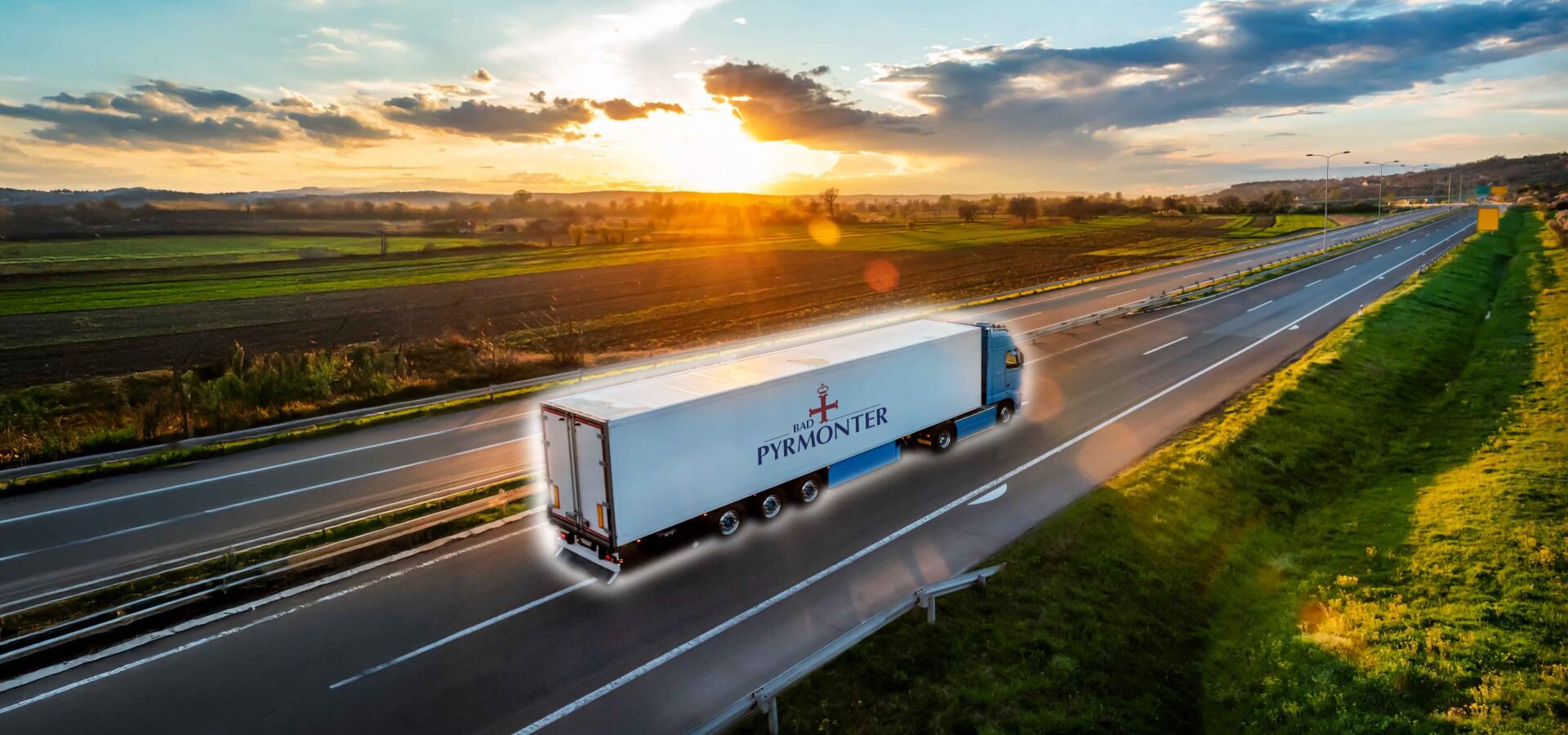 Lastwagen mit Bad Pyrmonter Logo fährt bei Sonnenuntergang auf der Autobahn durch die Landschaft.