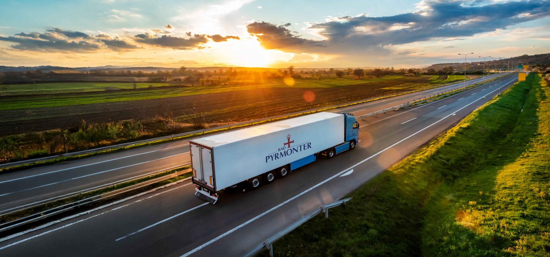 Lastwagen mit Bad Pyrmonter Logo fährt bei Sonnenuntergang auf der Autobahn durch die Landschaft.