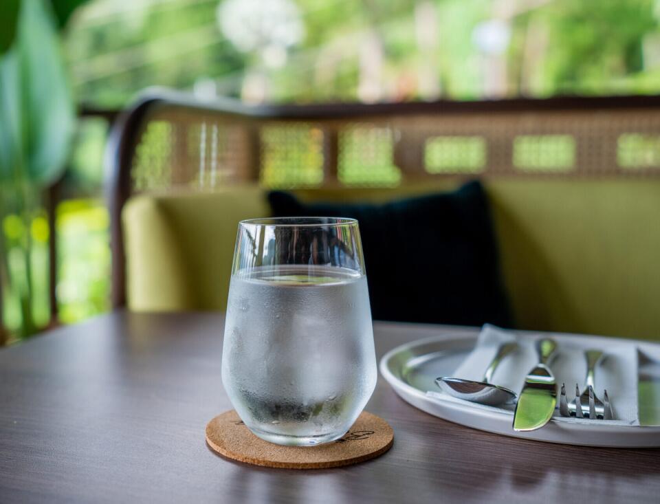 Ein Glas frisches Wasser auf einem gedeckten Tisch mit Teller und Besteck.