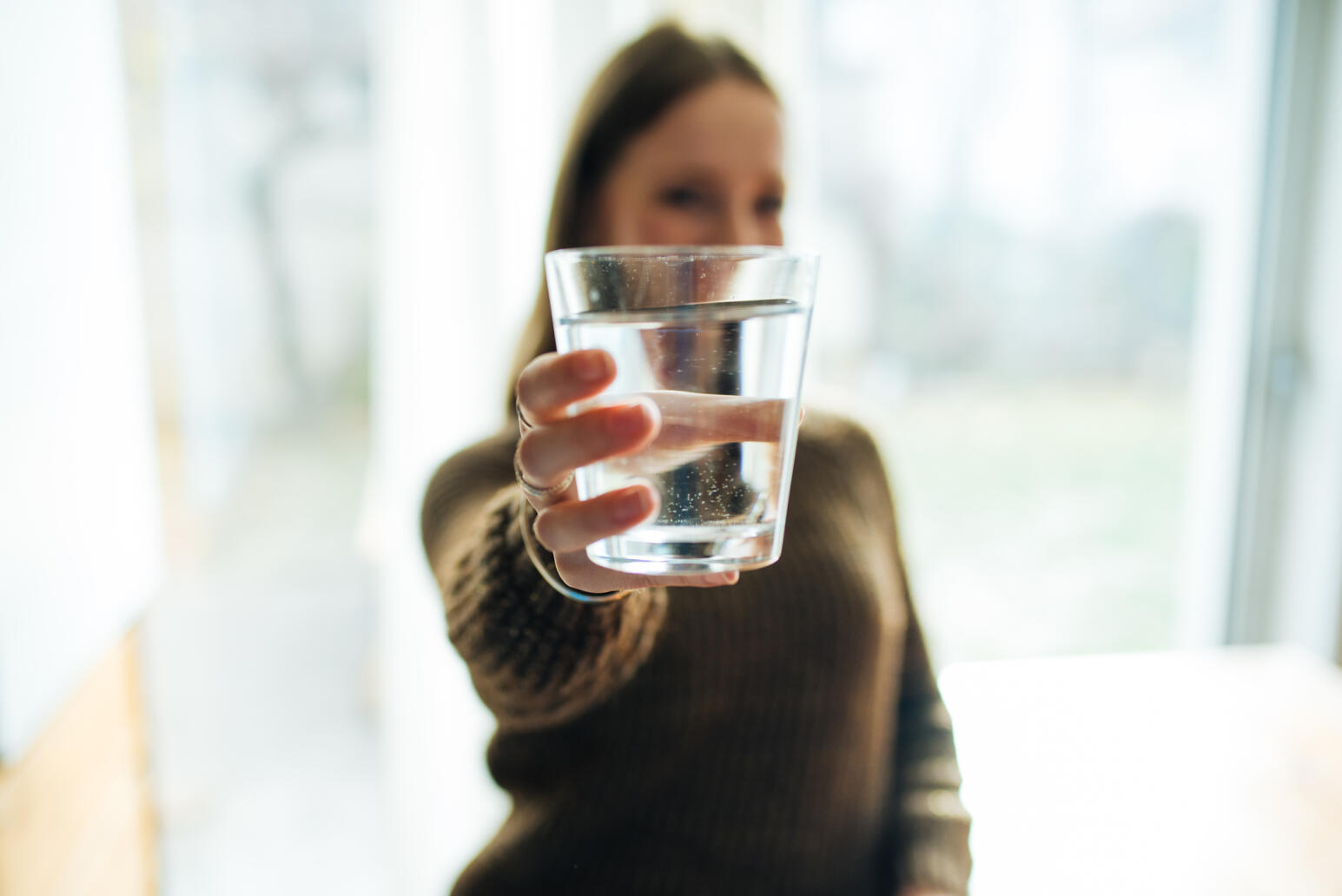Eine Frau hält ein Glas Wasser in die Kamera.