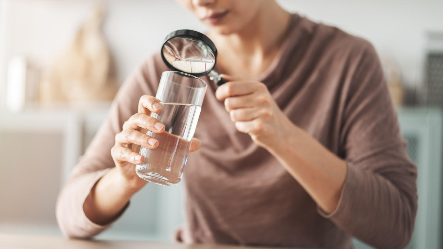 Frau untersucht Wasserglas mit Lupe