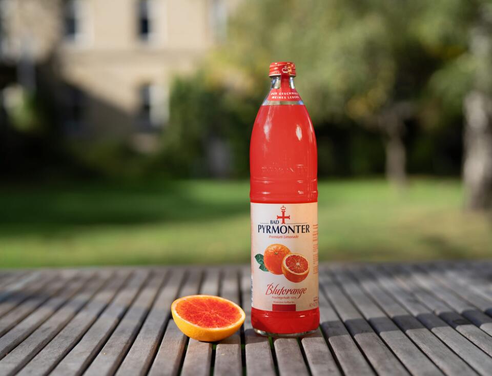 Bad Pyrmonter Premium Limonade Blutorange auf einem Holztisch vor Naturhintergrund.