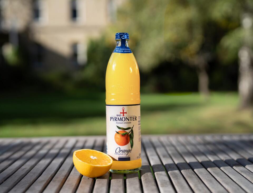 Bad Pyrmonter Premium Limonade Orange auf einem Holztisch vor Naturhintergrund.