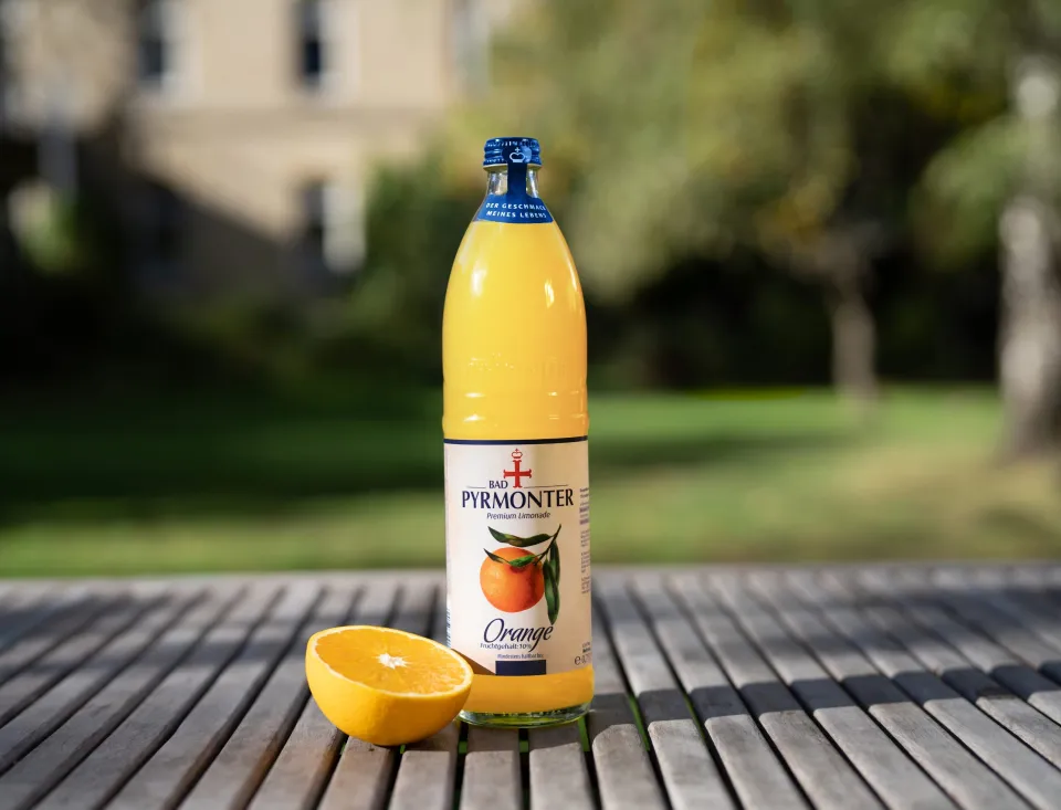 Bad Pyrmonter Premium Limonade Orange auf einem Holztisch vor Naturhintergrund.
