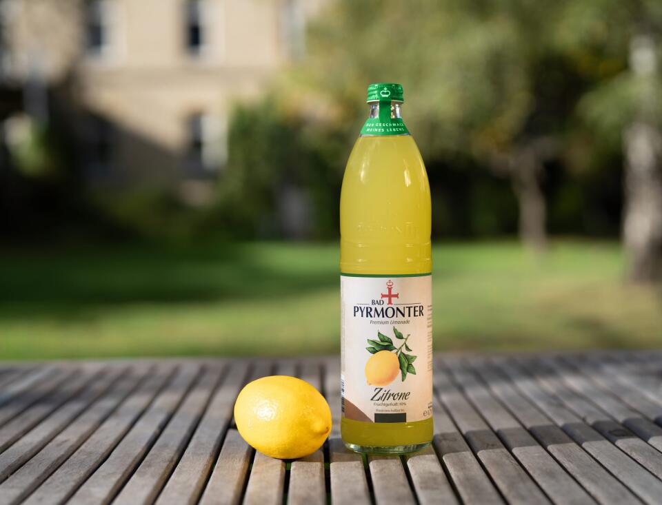 Bad Pyrmonter Premium Limonade Zitrone auf einem Holztisch vor Naturhintergrund.