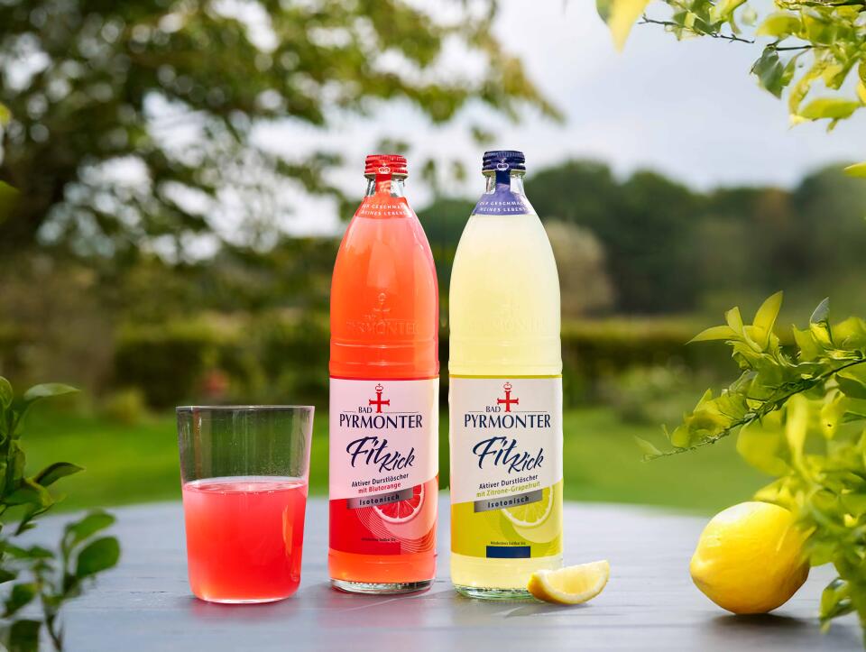 Zwei Flaschen Bad Pyrmonter FitKick in den Sorten Grapefruit und Zitrone mit Glas Getränk.
