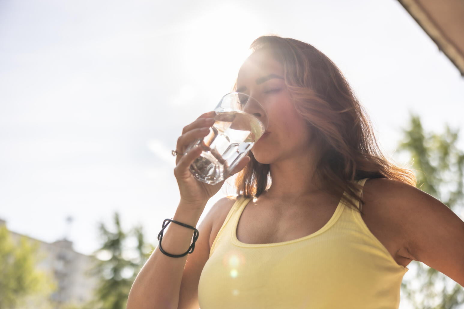 Frau trinkt nach sportlicher Aktivität in der Natur, Wasser aus einem Glas.