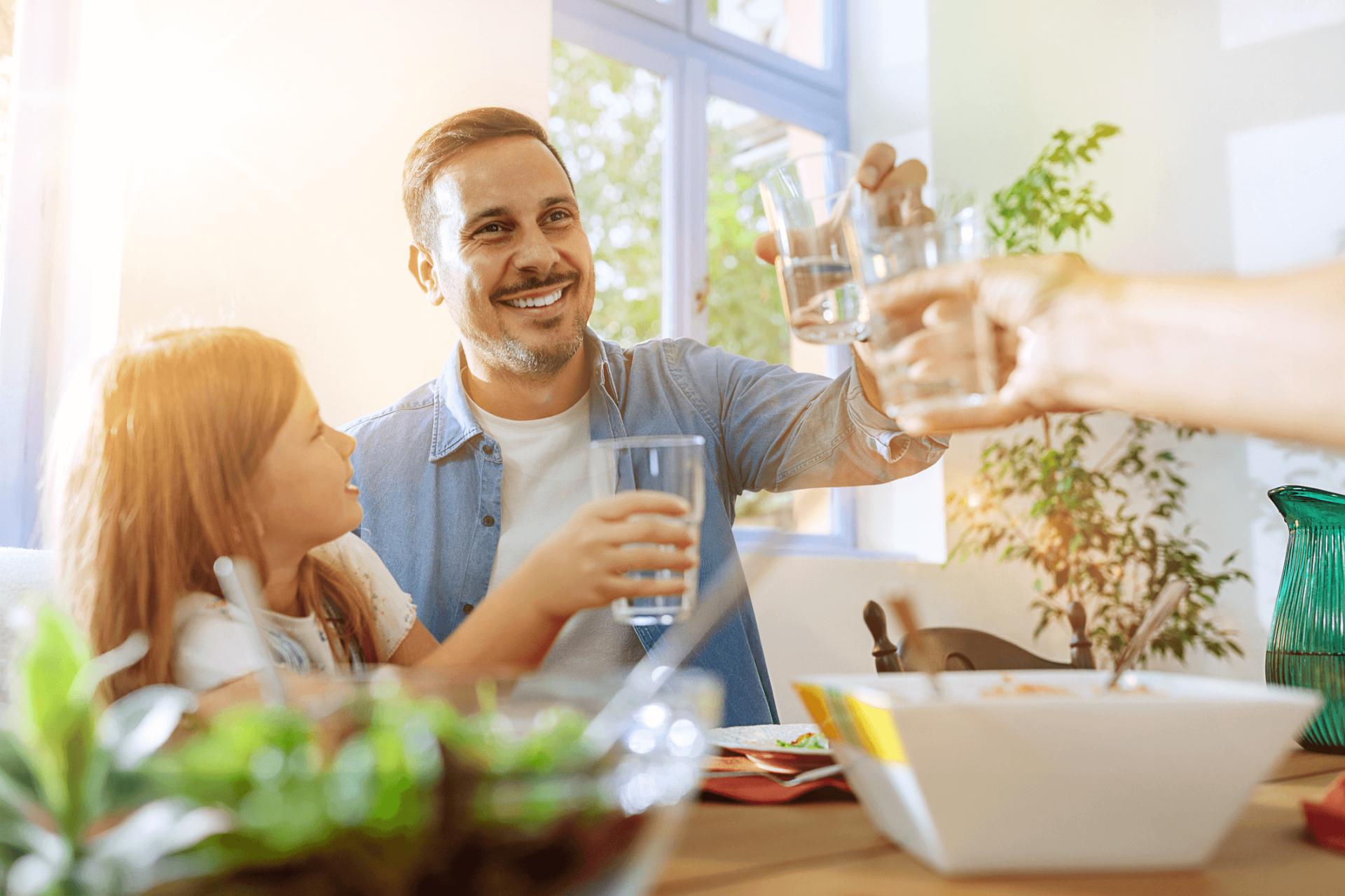 Eine Familie am Esstisch, die mit Wassergläsern anstößt
