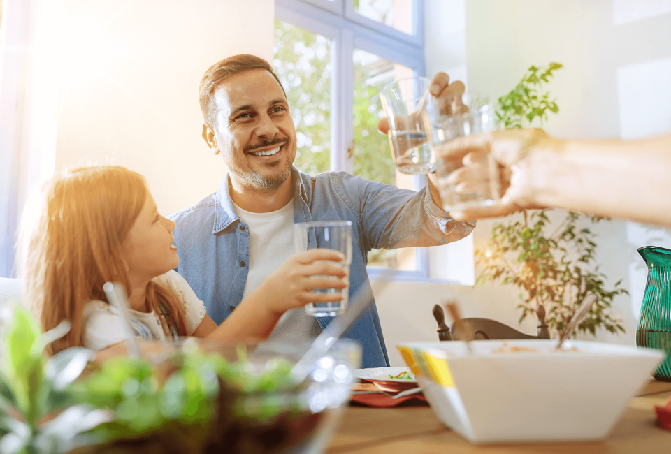 Eine Familie am Esstisch, die mit Wassergläsern anstößt