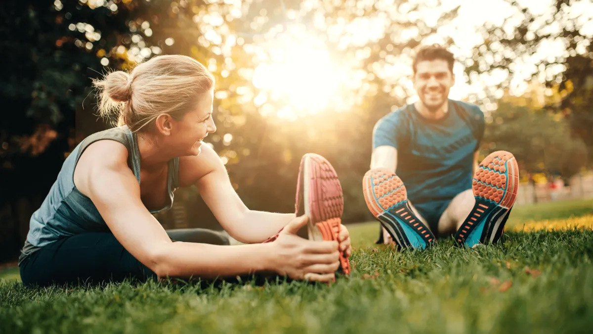 Ein Mann und eine Frau stretchen sich vor einem Lauf