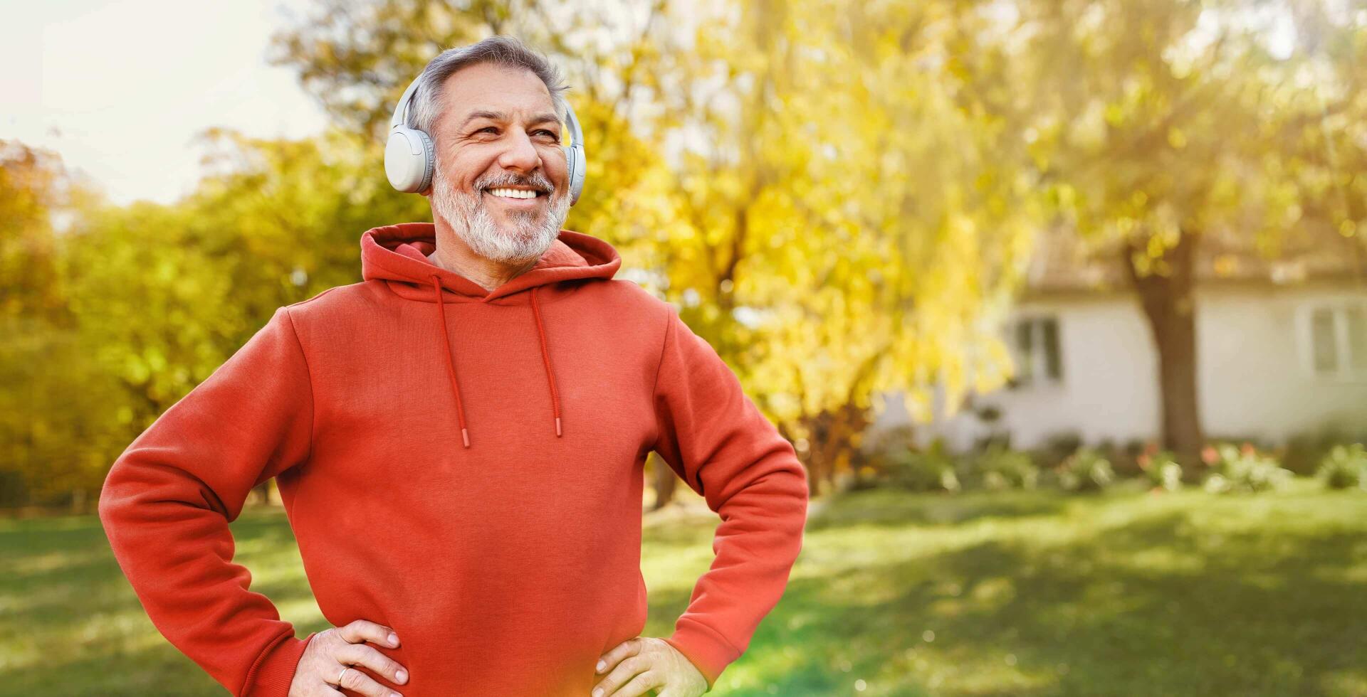 Ein Mann im roten Pullover hört mit seinem silbernen Kopfhörer Musik in einem Garten