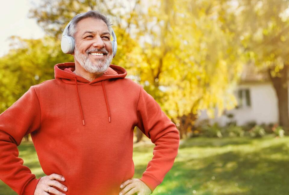 Ein Mann im roten Pullover hört mit seinem silbernen Kopfhörer Musik in einem Garten