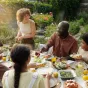 Eine Gruppe Menschen sitzt in einem schönen Garten an einem gedeckte Tisch und isst gemeinsam