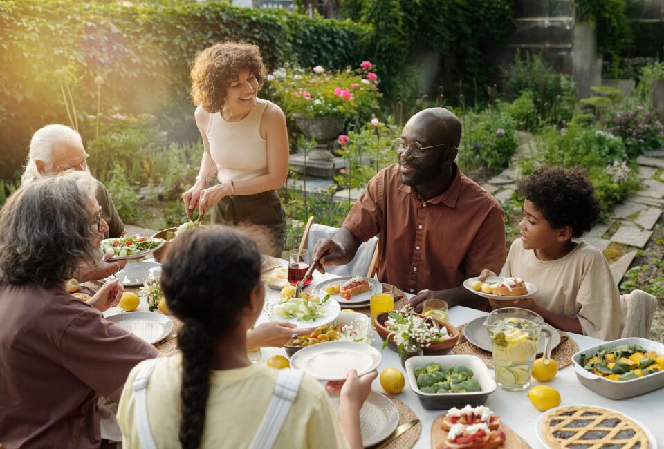 Eine Gruppe Menschen sitzt in einem schönen Garten an einem gedeckte Tisch und isst gemeinsam