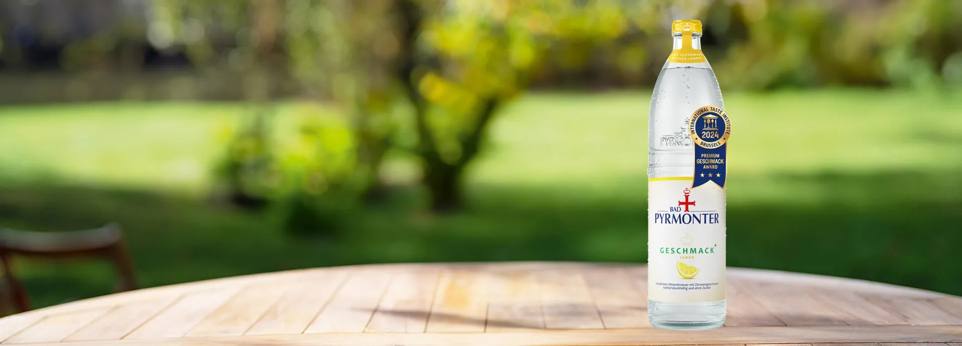Eine Glasflasche Bad Pyrmonter Geschmack Plus Lemon auf einem Tisch vor einem Naturhintergrund mit einer Auszeichnung