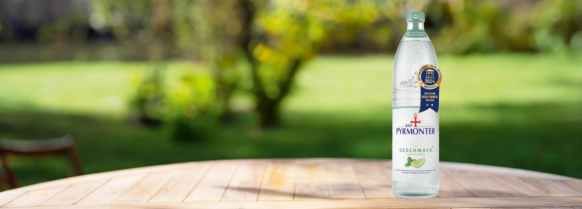 Eine Glasflasche Bad Pyrmonter Geschmack Plus Limette-Minze auf einem Tisch vor einem Naturhintergrund mit einer Auszeichnung