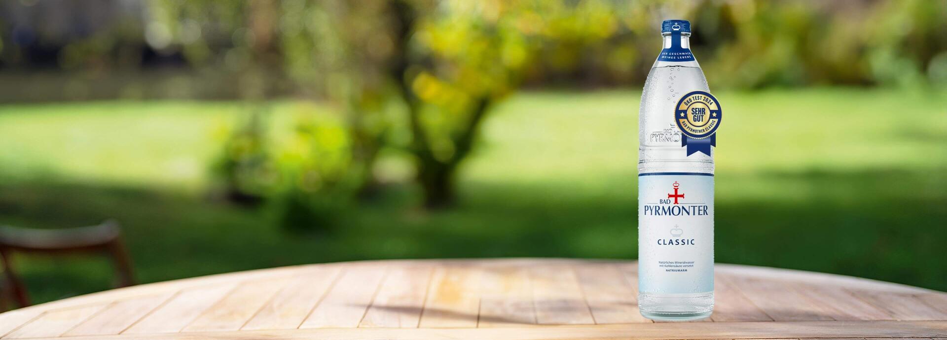 Eine Glasflasche Bad Pyrmonter Classic auf einem Tisch vor einem Naturhintergrund mit einer Öko-Test Auszeichnung