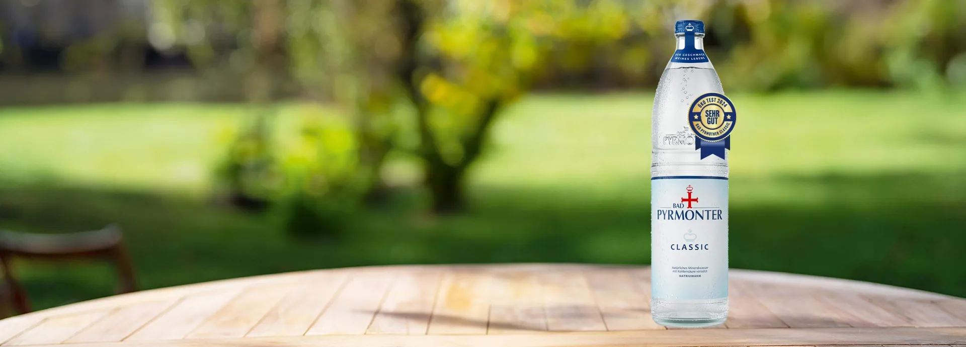 Eine Glasflasche Bad Pyrmonter Classic auf einem Tisch vor einem Naturhintergrund mit einer Öko-Test Auszeichnung