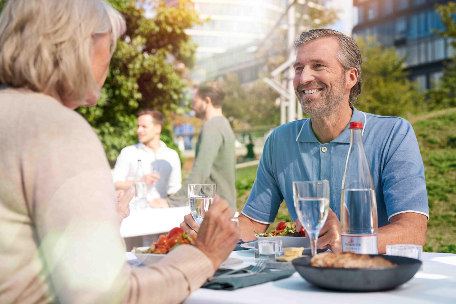 Älteres Paar genießt ein Mittagessen im Freien mit Wasser und Essen.